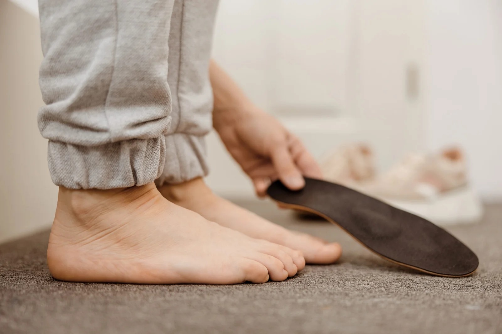 Patient holding a custom prescription shoe insert next to bare feet, showcasing podiatric orthotics therapy.